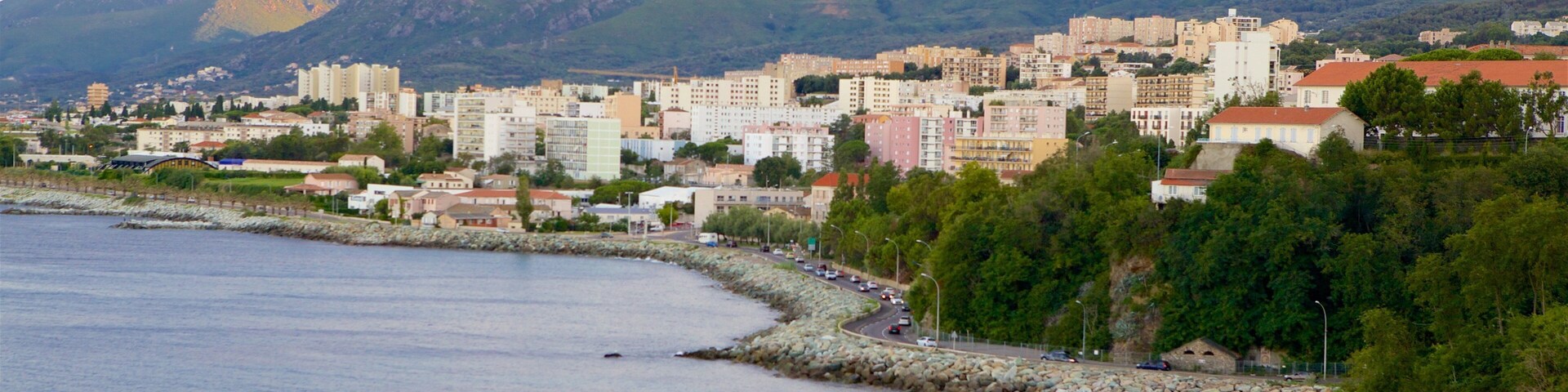 Una ciudad costera con un litoral rocoso, una carretera a lo largo de la costa y montañas al fondo.