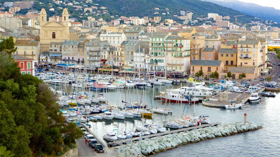 A marina filled with boats, surrounded by colorful buildings and a mountainous backdrop.