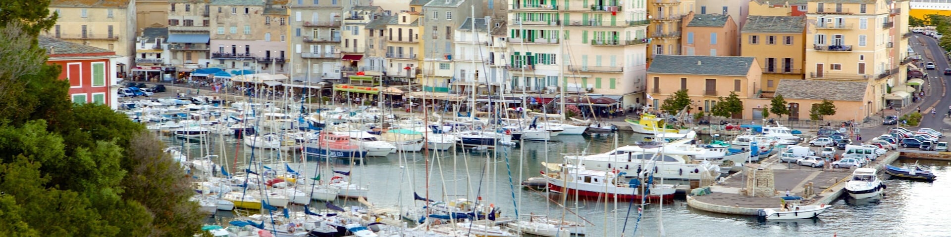 A marina filled with boats, surrounded by colorful buildings and a mountainous backdrop.