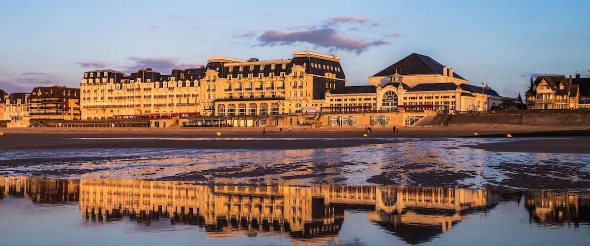 Un paisaje urbano frente al mar con aguas reflectantes, edificios históricos y cielo despejado.