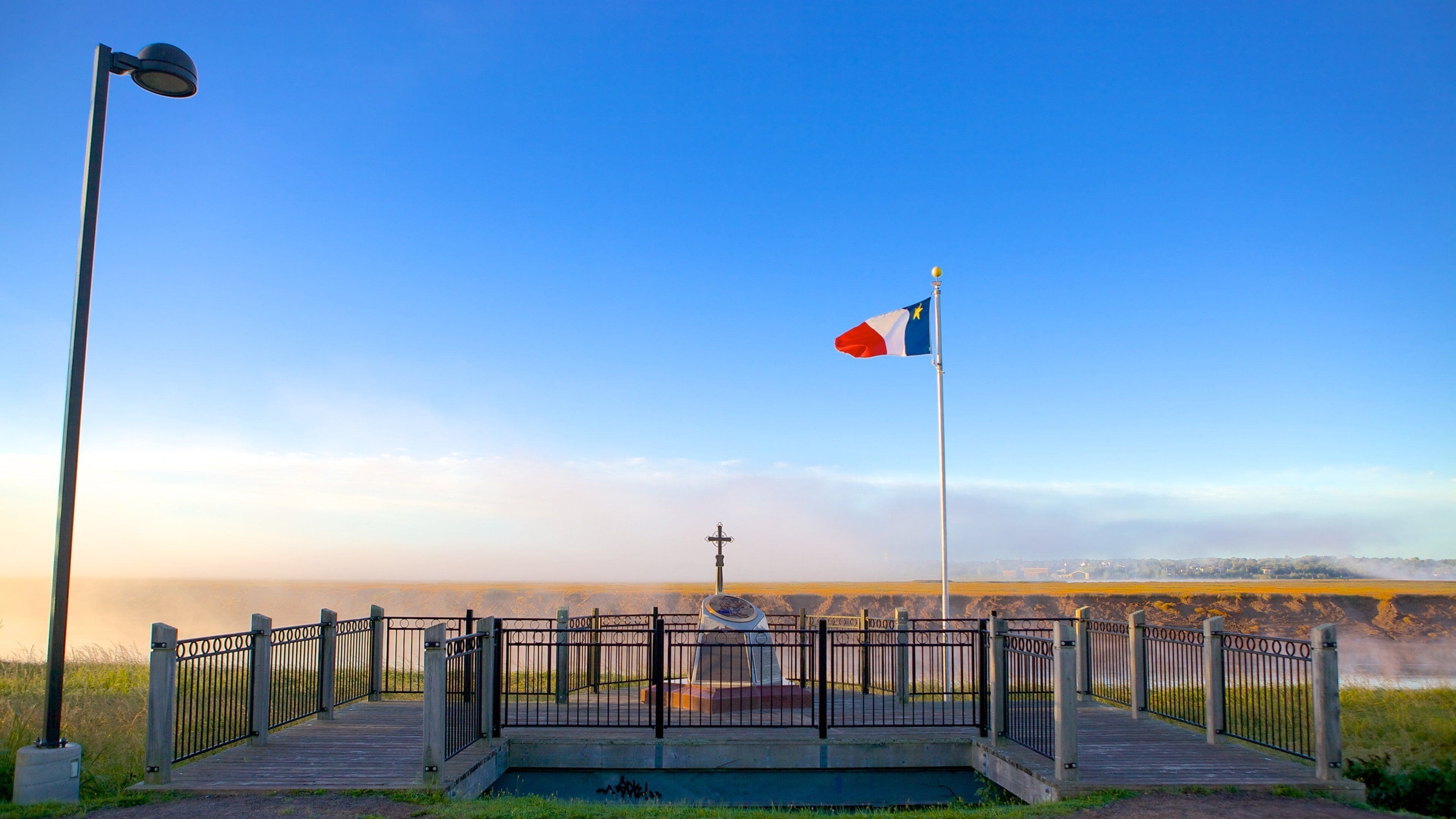 A memorial with a flag, a cross, and a wooden walkway.