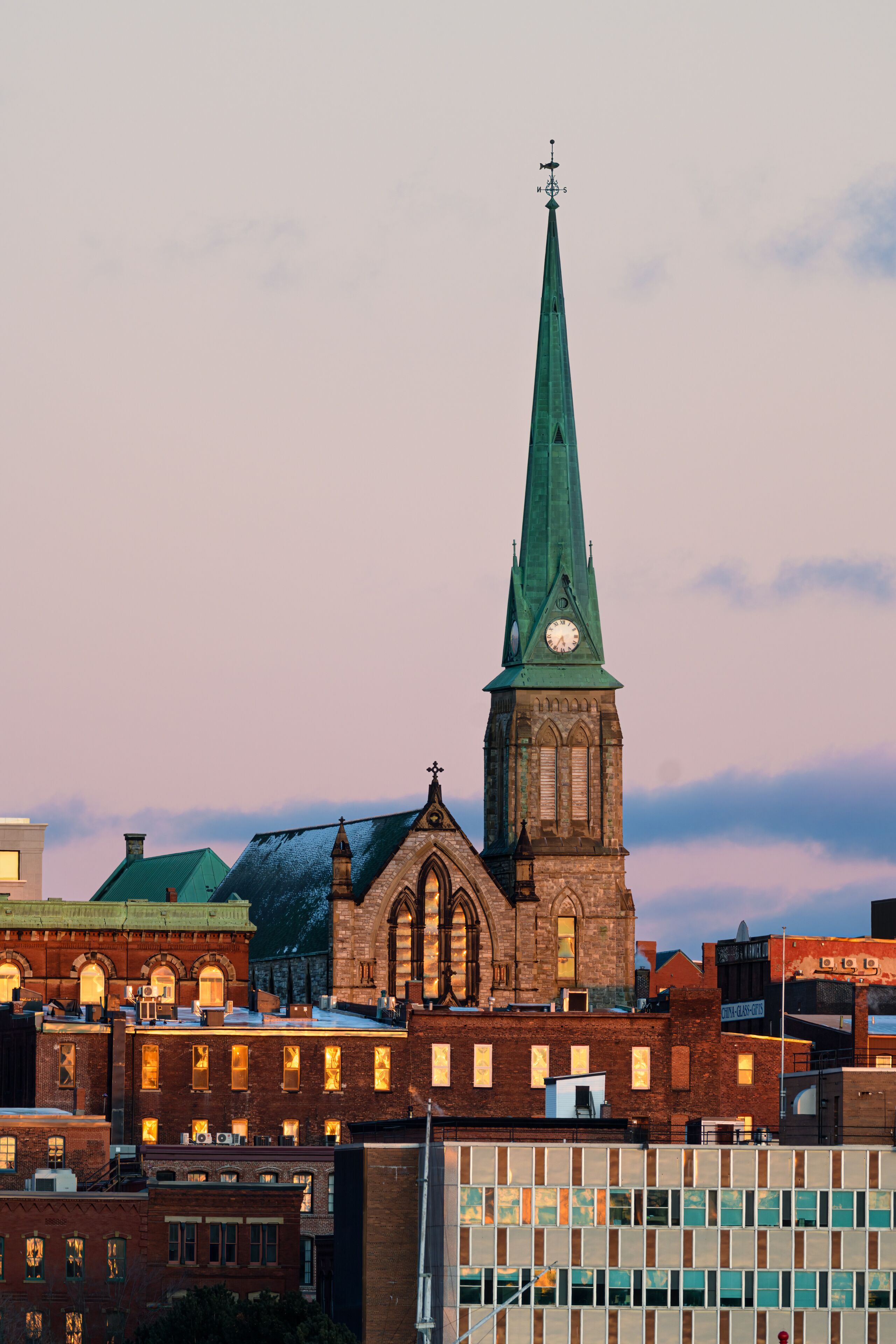 Uma igreja com uma torre alta e um relógio, rodeada por edifícios urbanos.