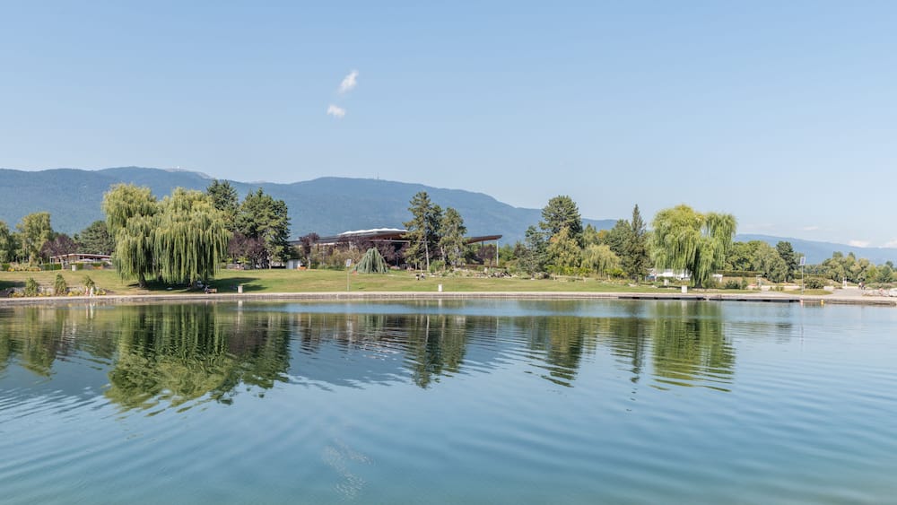 A calm lake with reflections of trees and a building in the background.