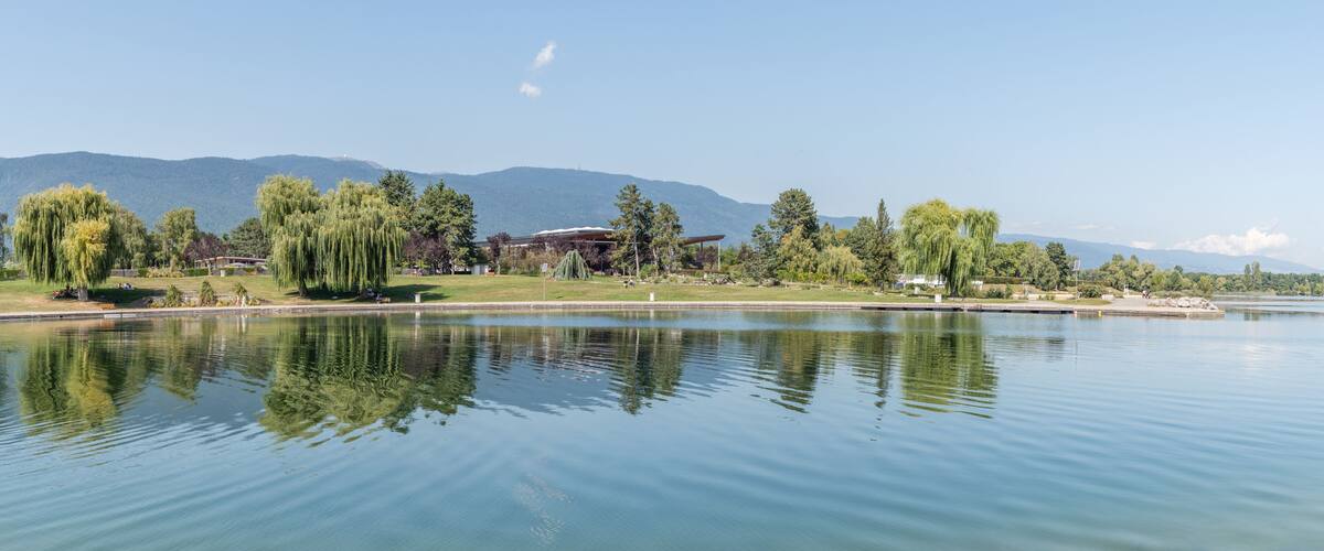 A calm lake with reflections of trees and a building in the background.