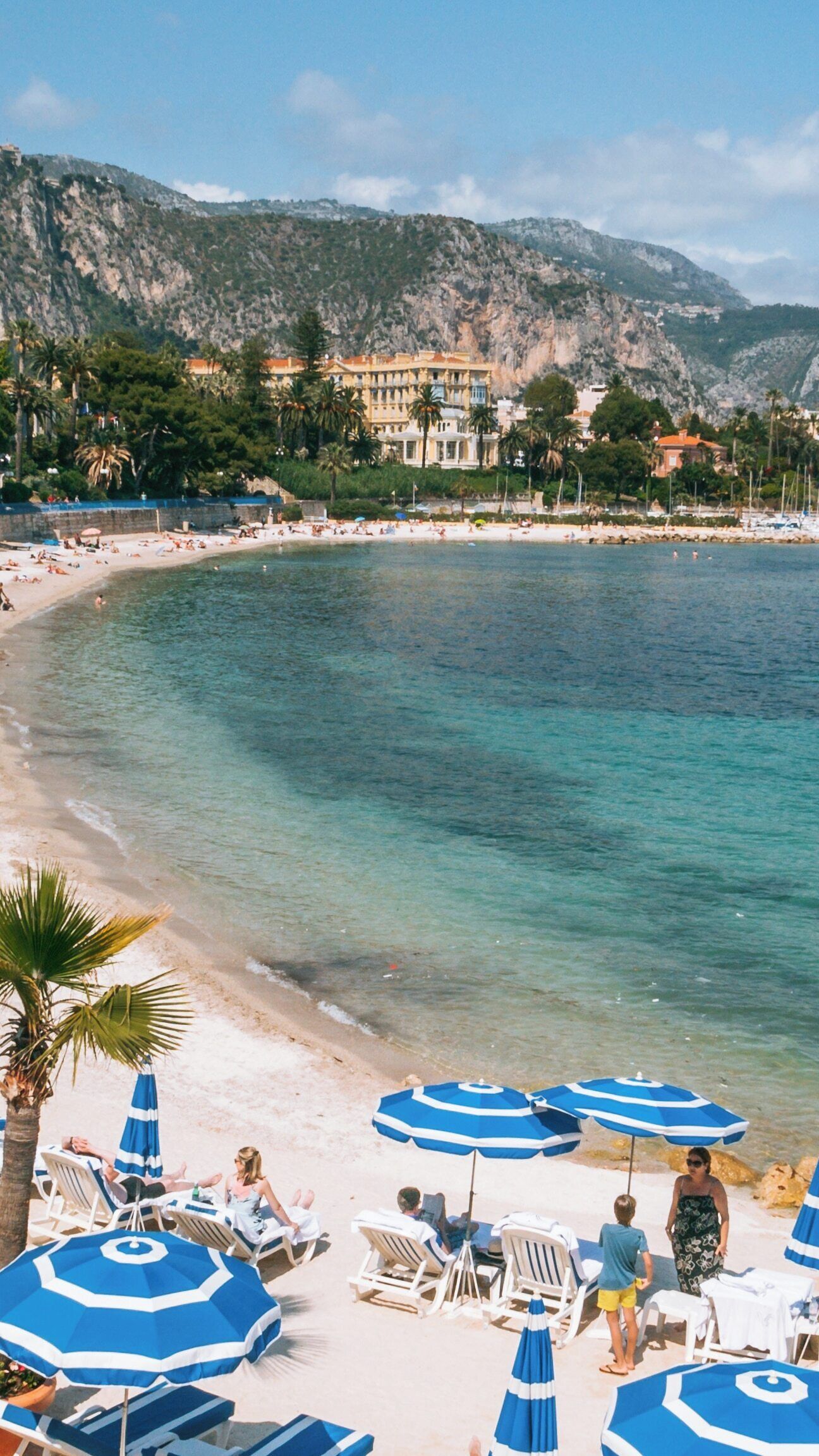 Una playa con agua turquesa cristalina, arena blanca y sombrillas azules.
