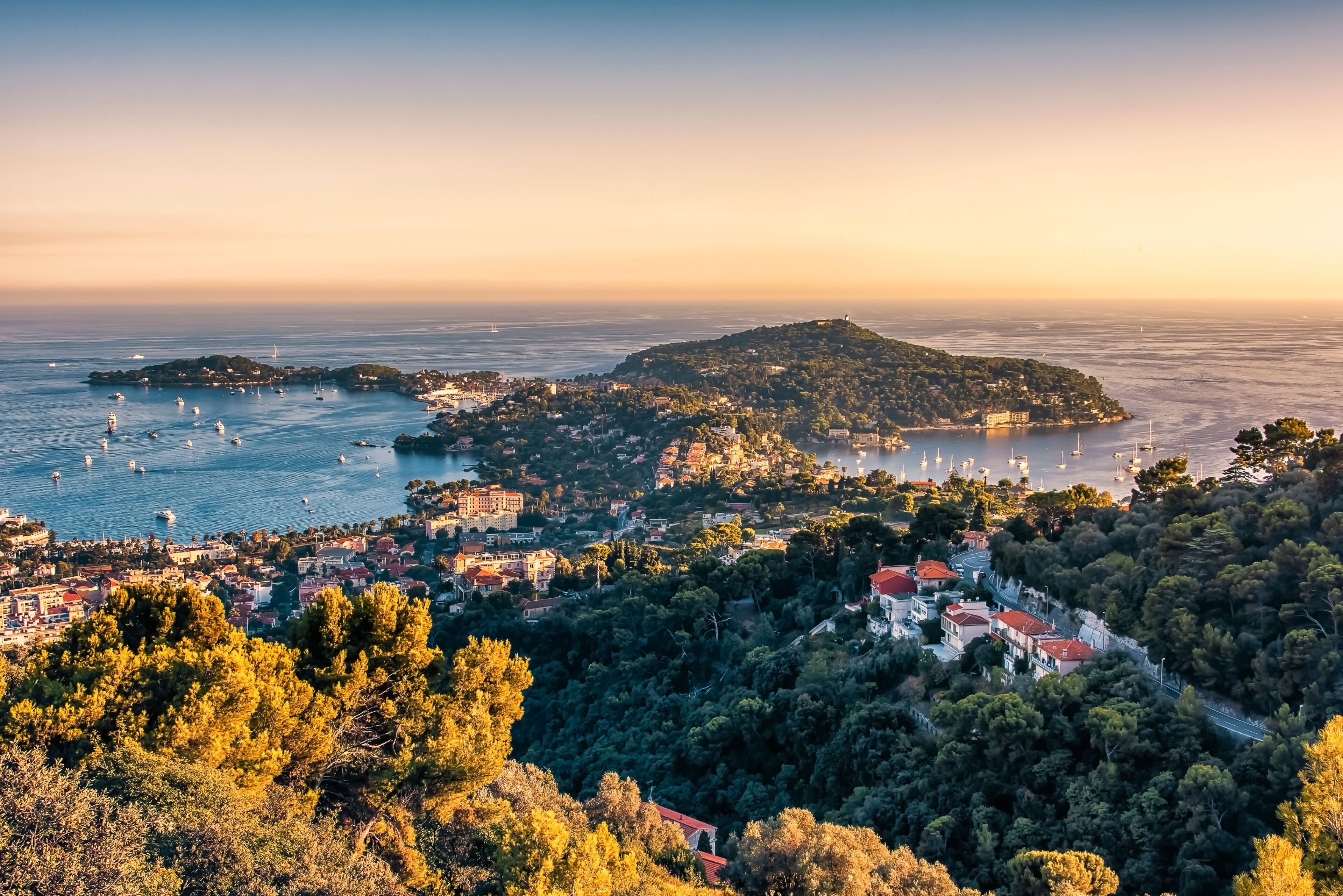 A coastal town with a hilly backdrop, a marina with boats, and dense greenery.