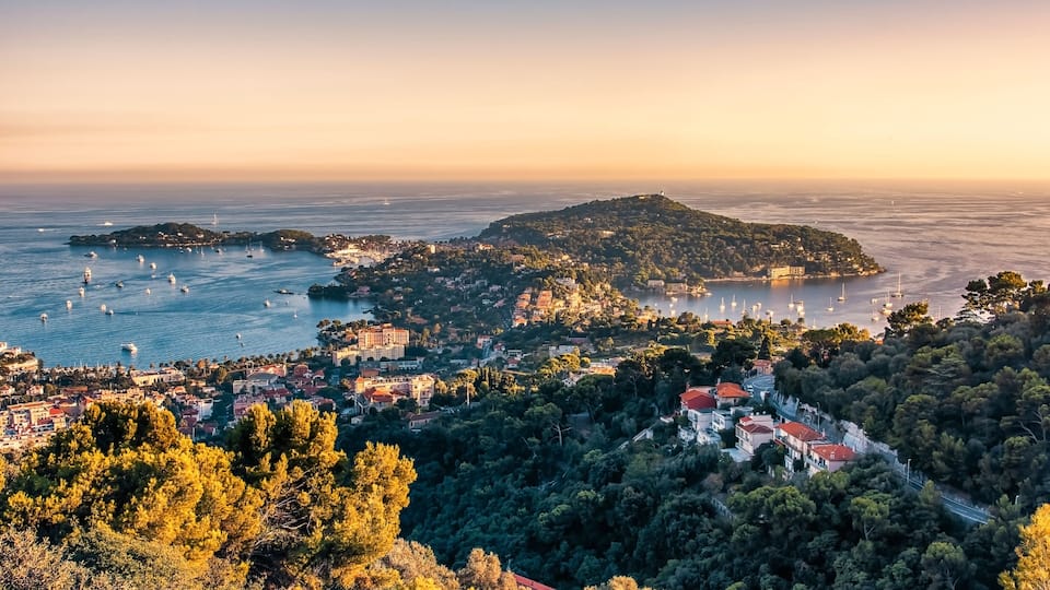 A coastal town with a hilly backdrop, a marina with boats, and dense greenery.