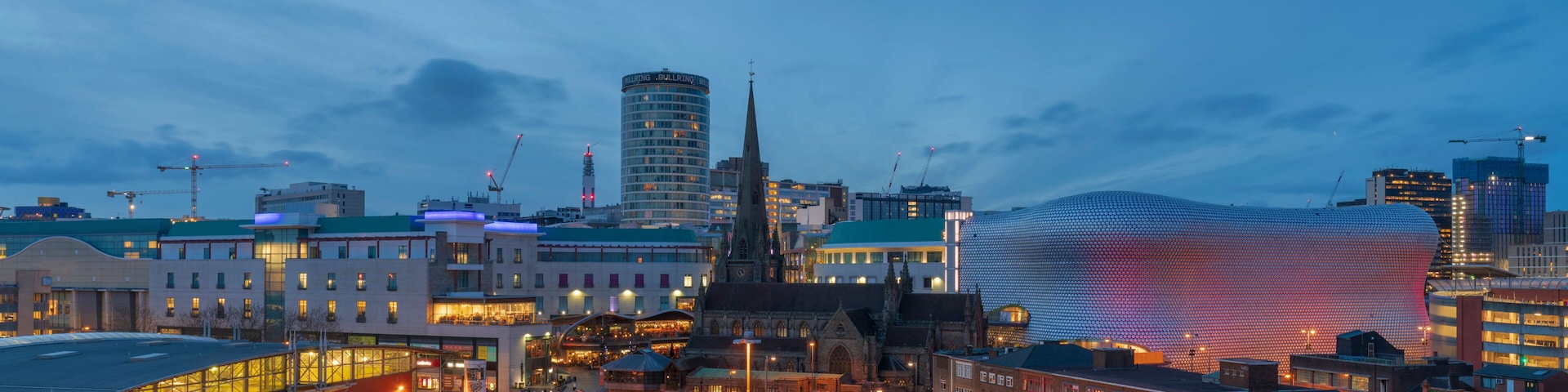 Une vue d’une ville au crépuscule, avec un bâtiment sphérique remarquable et le clocher imposant d’une église.