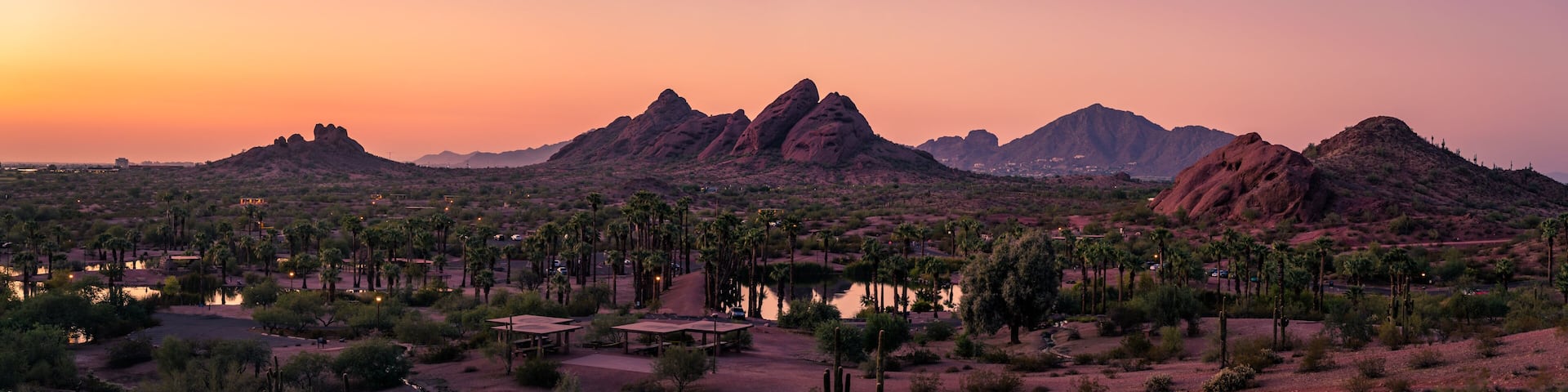A desert landscape with prominent rock formations and a small settlement with palm trees.