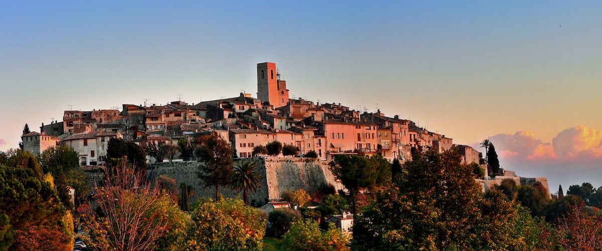 A historic town with a prominent tower, surrounded by lush greenery and a stone wall.