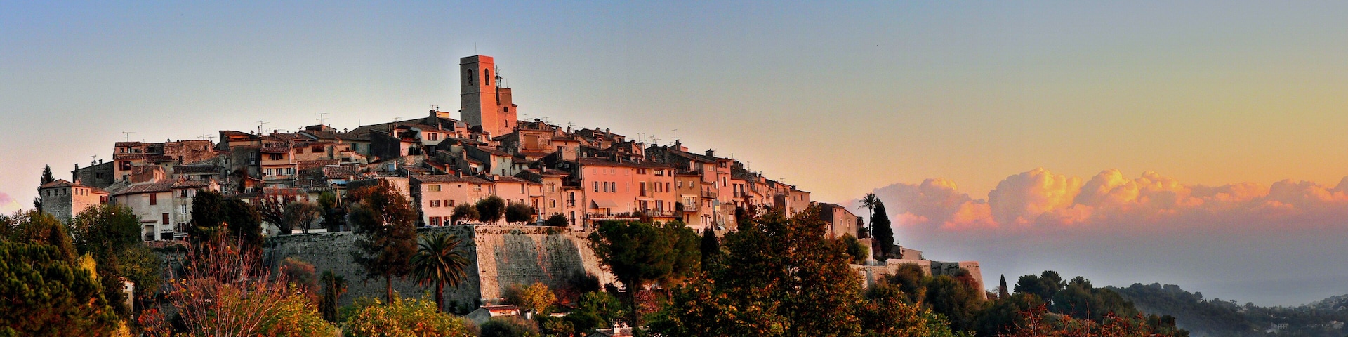 A historic town with a prominent tower, surrounded by lush greenery and a stone wall.