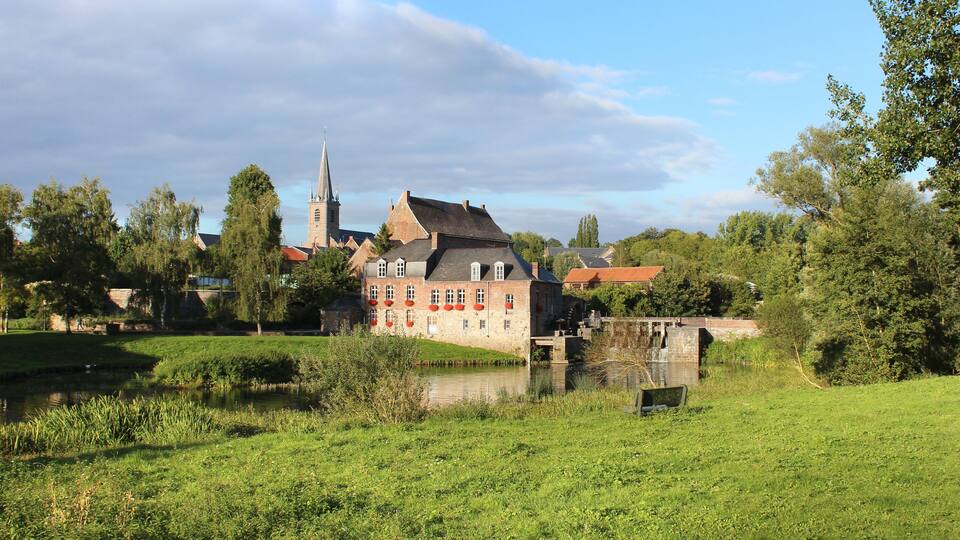 A historic building with a tower, surrounded by lush greenery and a small pond.