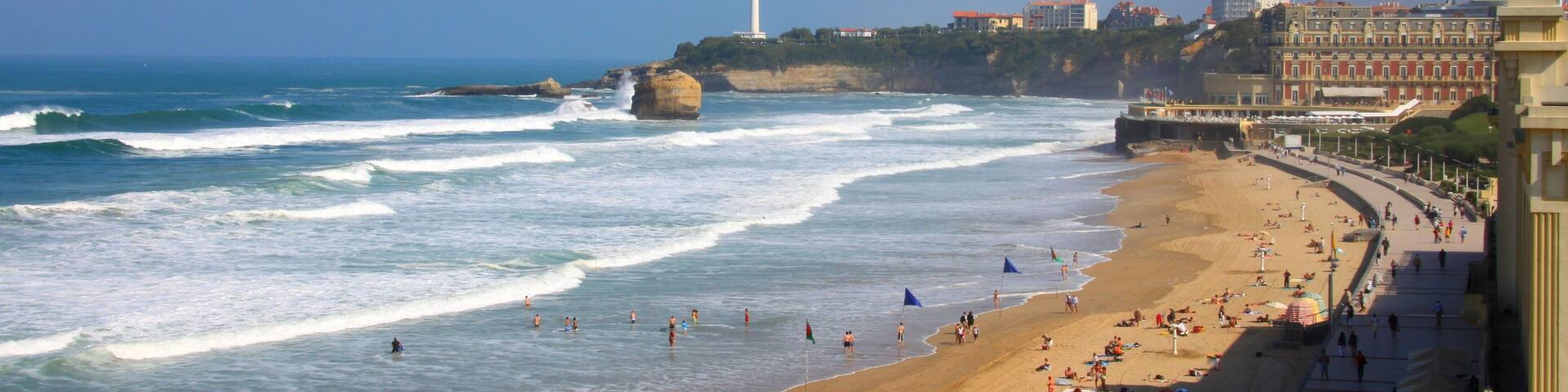 A coastal cityscape with a beach, waves, a lighthouse, and buildings.