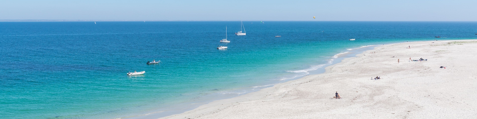 Una playa con arena blanca, agua turquesa cristalina y varios barcos anclados cerca de la orilla.