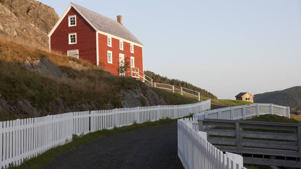 A red barn on a hillside with a white picket fence.