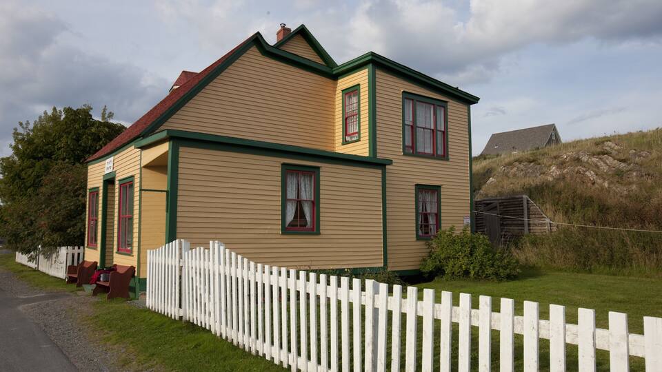A two-story house with a red roof and green trim, surrounded by a white picket fence.