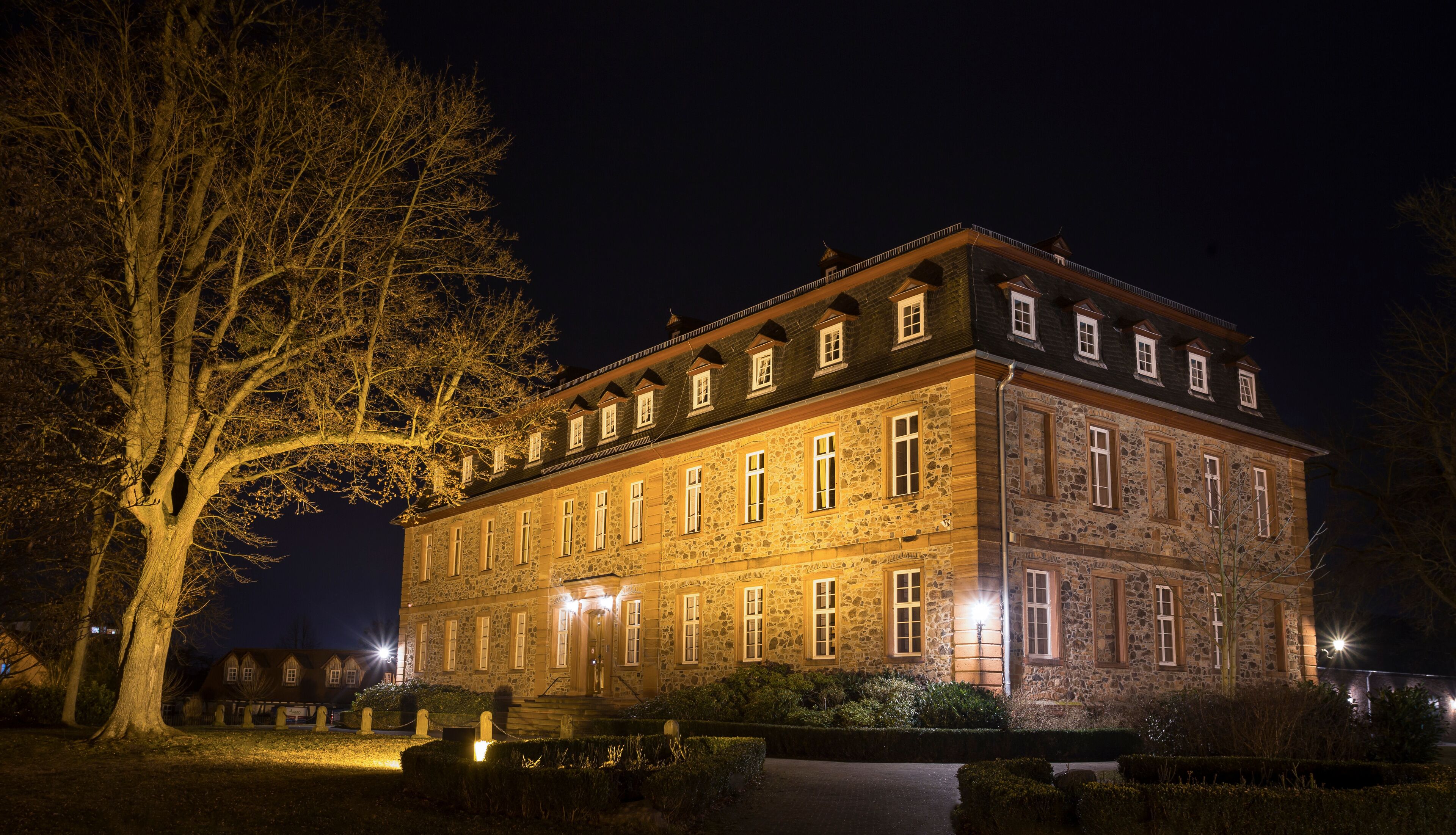 A large stone building with multiple windows and a prominent tree in the foreground.