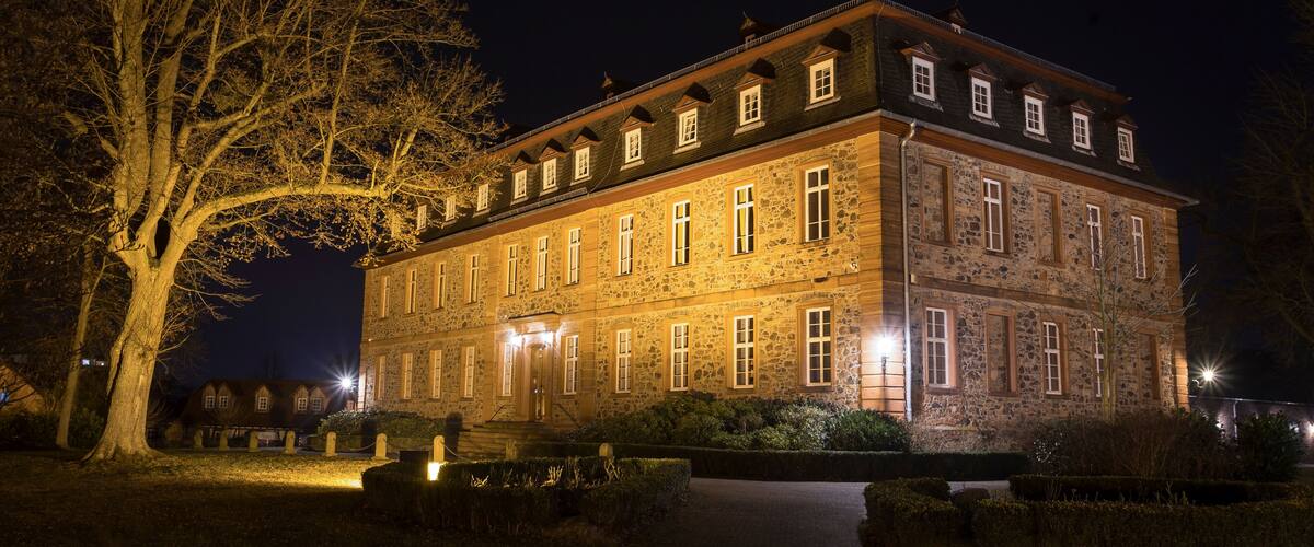 A large stone building with multiple windows and a prominent tree in the foreground.