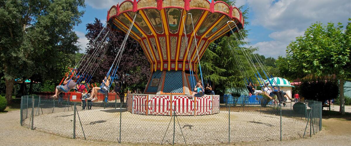 A carousel with a blue canopy and red and yellow stripes, surrounded by a fence.
