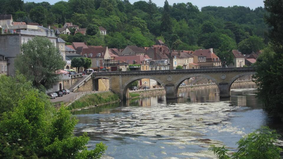 A river with a stone bridge, surrounded by buildings and greenery.