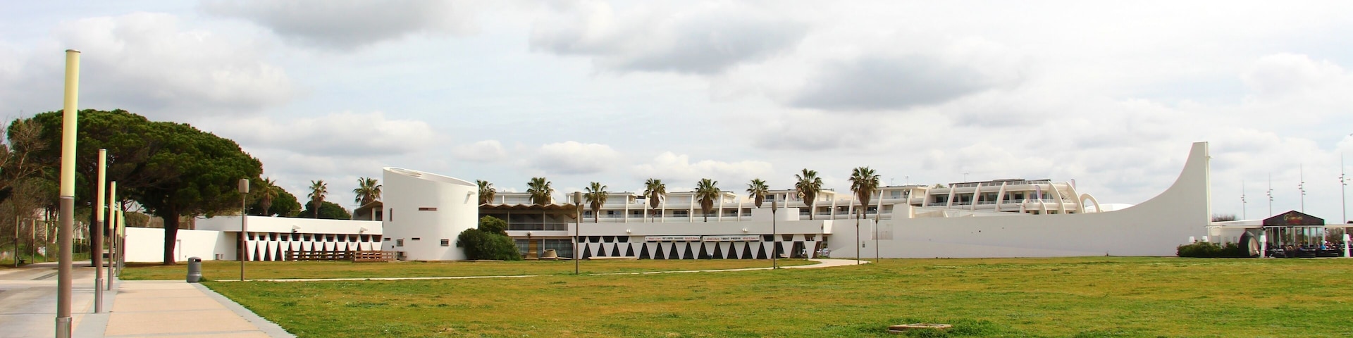 Point Zéro|Allée de la Plage Emblematic curved building of La Grande-Motte, it is behind the dune which gave its name to the resort (dune that was higher than the others). This building, whose uses have changed since its implementation, now houses a shopping centre and a leisure centre. Arch. Jean Balladur and Jean-Bernard Tostivint 1970.