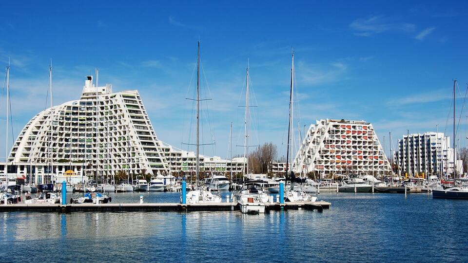 A marina with sailboats and modern buildings with unique architecture.