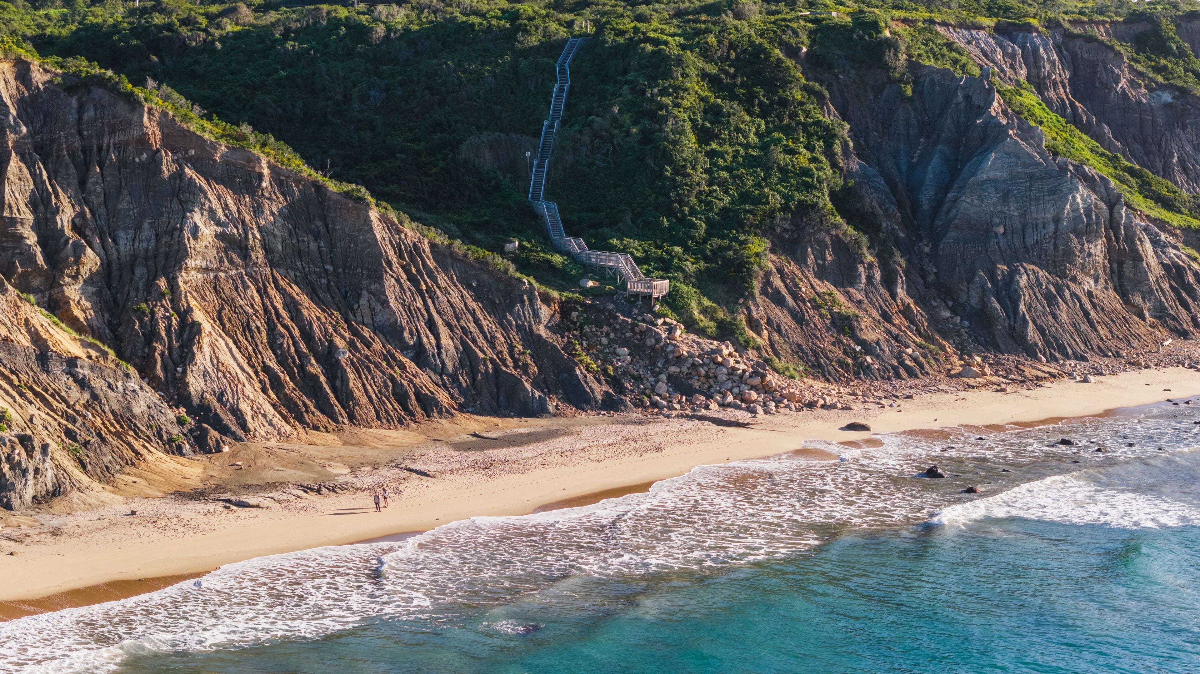 Un paisaje costero con una playa arenosa, un acantilado rocoso y una cascada.