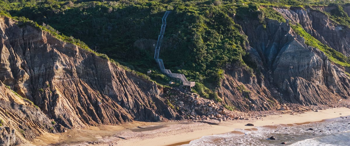 A coastal landscape with a sandy beach, a rocky cliff, and a waterfall.
