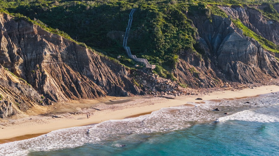 Un paisaje costero con una playa arenosa, un acantilado rocoso y una cascada.