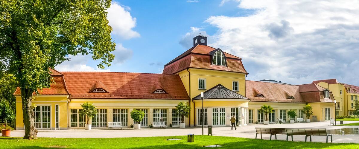 A historic building with a red-tiled roof and yellow walls, surrounded by a well-maintained lawn and a fountain.