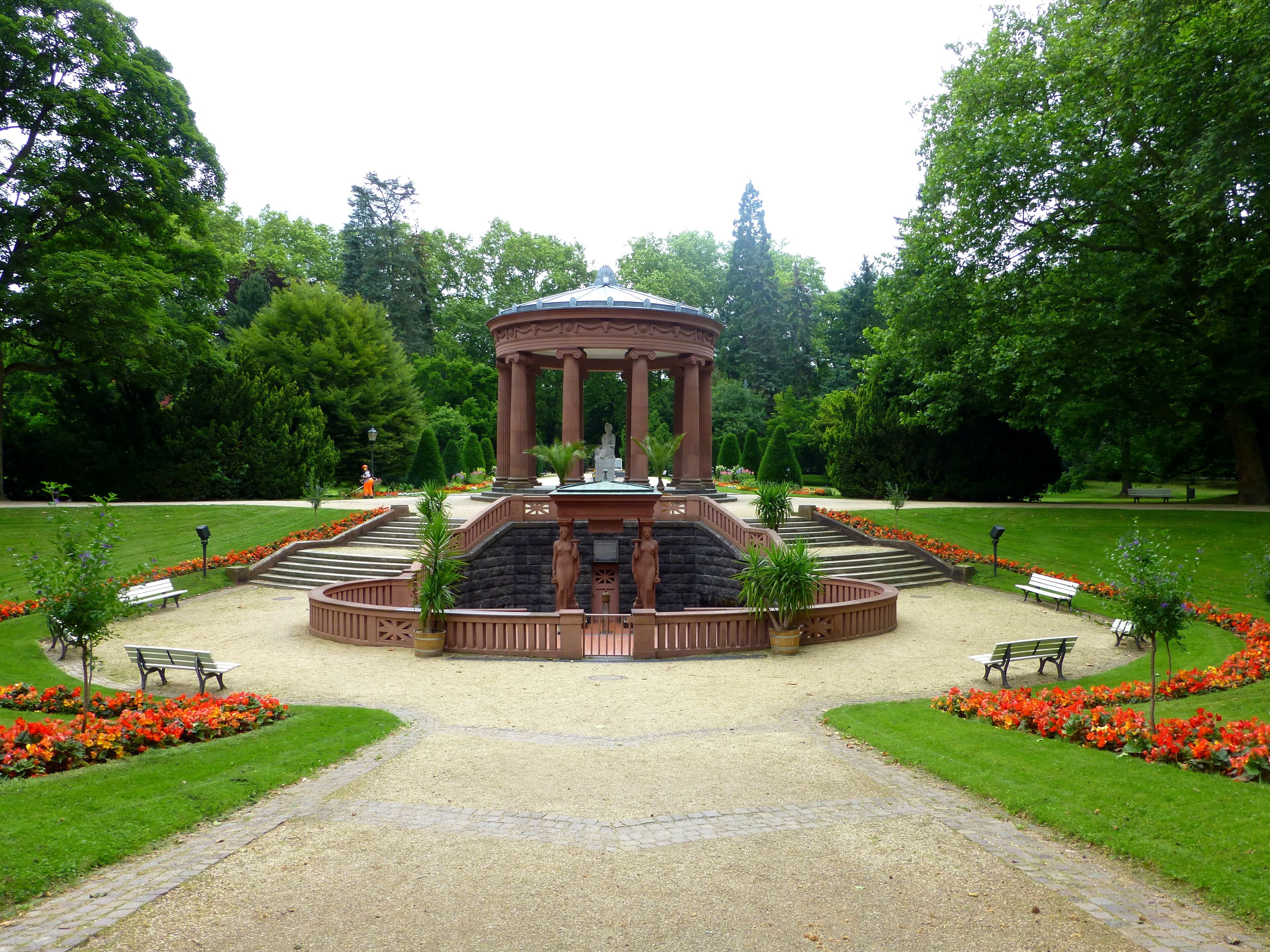A park with a central gazebo, surrounded by flower beds and benches.