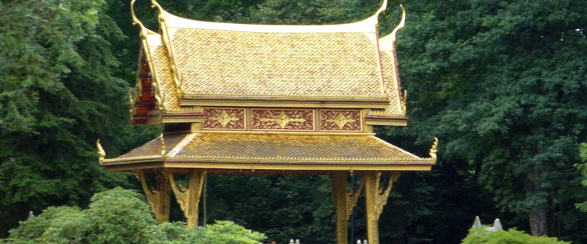 A golden pavilion with intricate designs, surrounded by lush green trees.