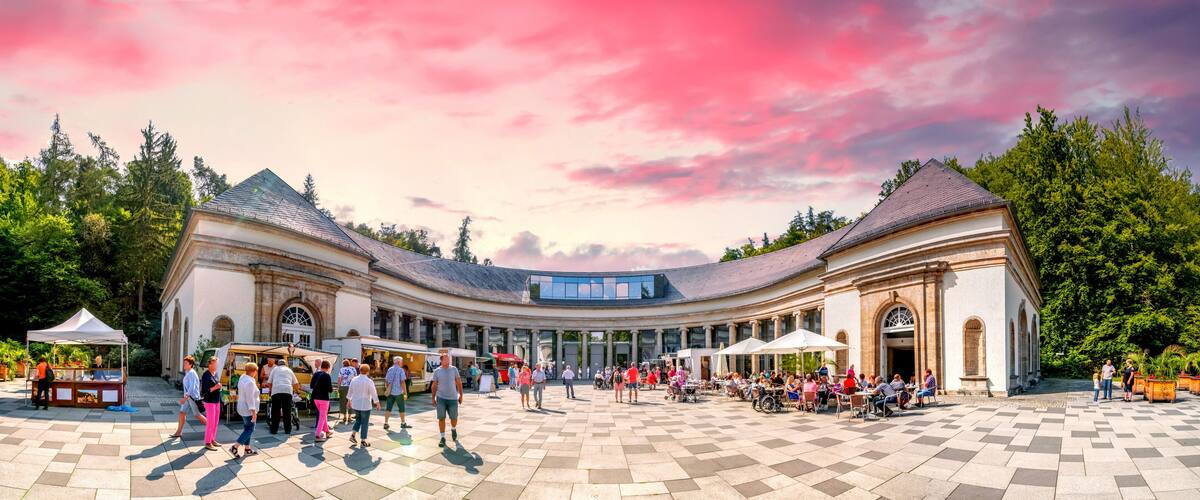 A spacious courtyard with a curved building, outdoor cafes, and a clear sky.