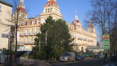 A large, ornate building with multiple domes and towers, surrounded by trees and parked cars.