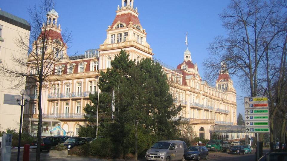 A large, ornate building with multiple domes and towers, surrounded by trees and parked cars.