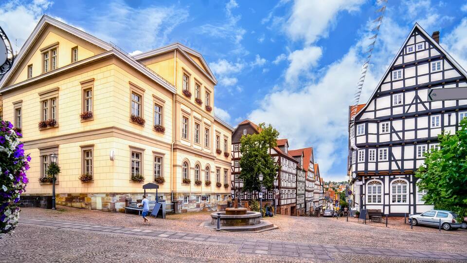 A cobblestone square with historic buildings, including a yellow building with arched windows and a half-timbered structure.