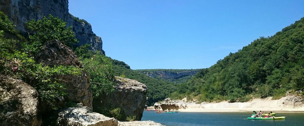 A river with kayakers, rocky cliffs, and dense greenery.