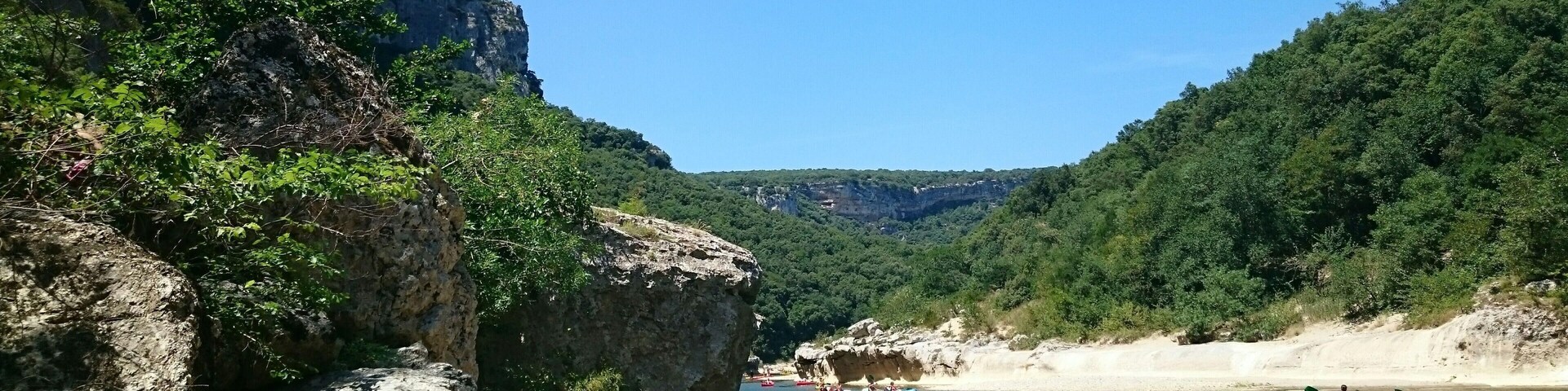 A river with kayakers, rocky cliffs, and dense greenery.