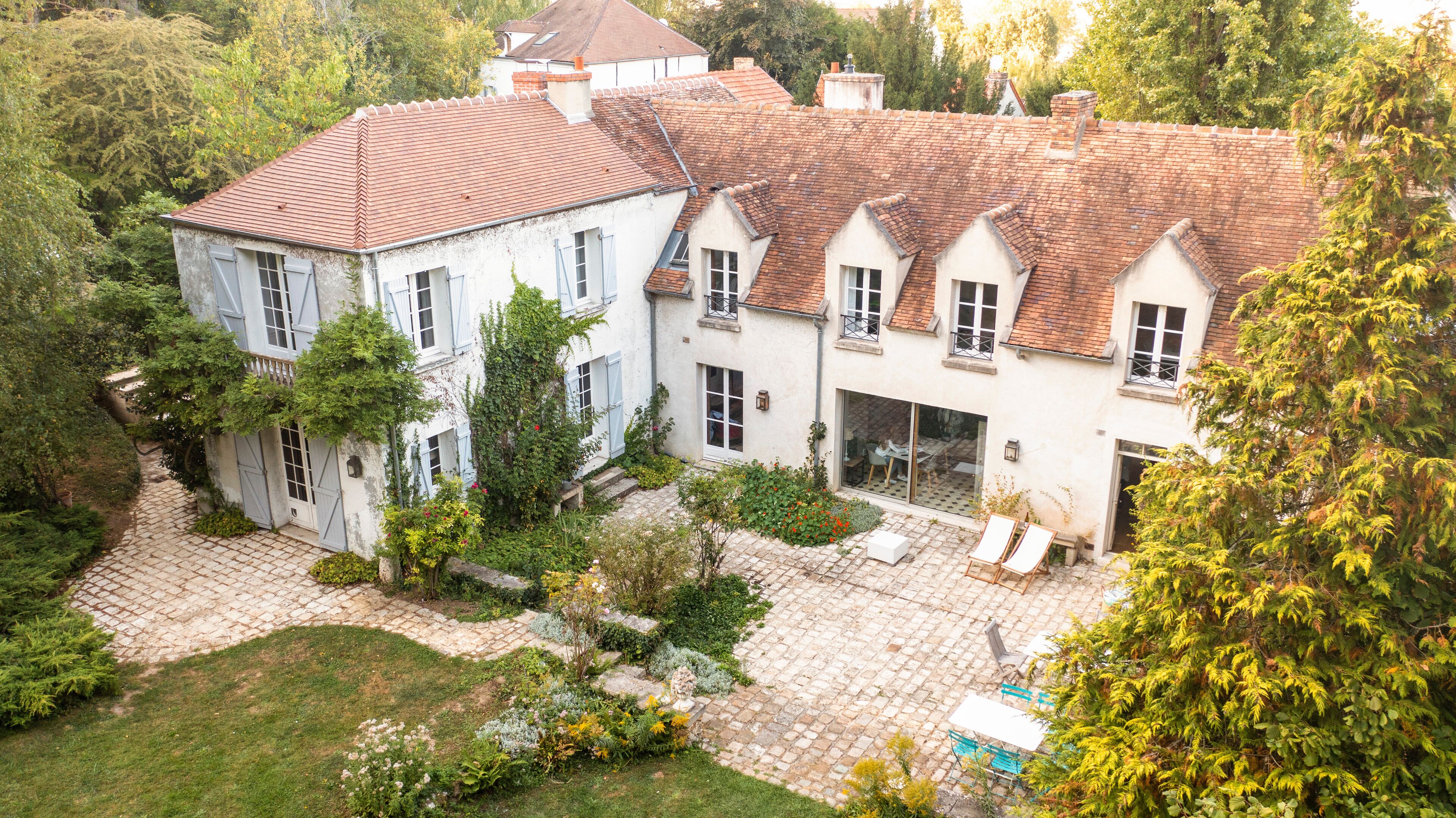 A large, white building with a red-tiled roof surrounded by lush greenery and a cobblestone courtyard.