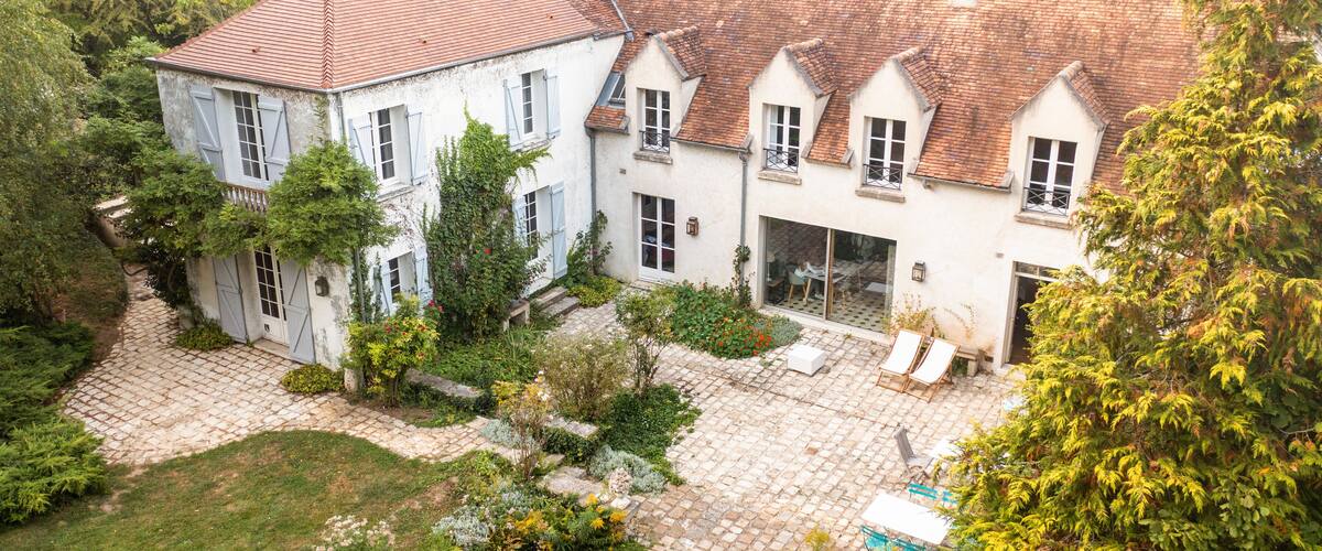A large, white building with a red-tiled roof surrounded by lush greenery and a cobblestone courtyard.