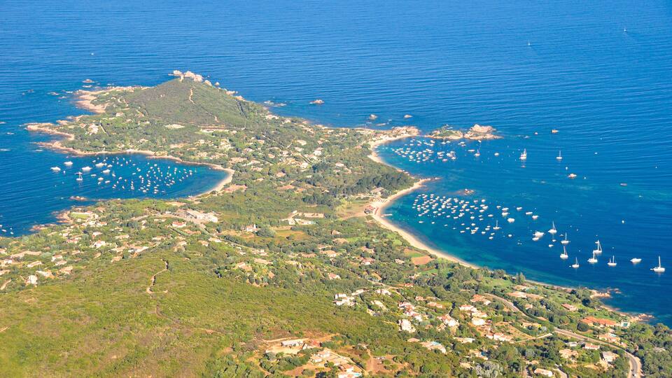An aerial view of a coastal town with a bay, numerous boats, and scattered buildings.