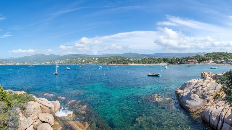 A coastal landscape with clear turquoise waters, rocky shores, and boats.