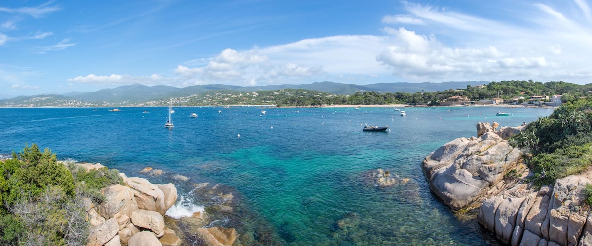 A coastal landscape with clear turquoise waters, rocky shores, and boats.