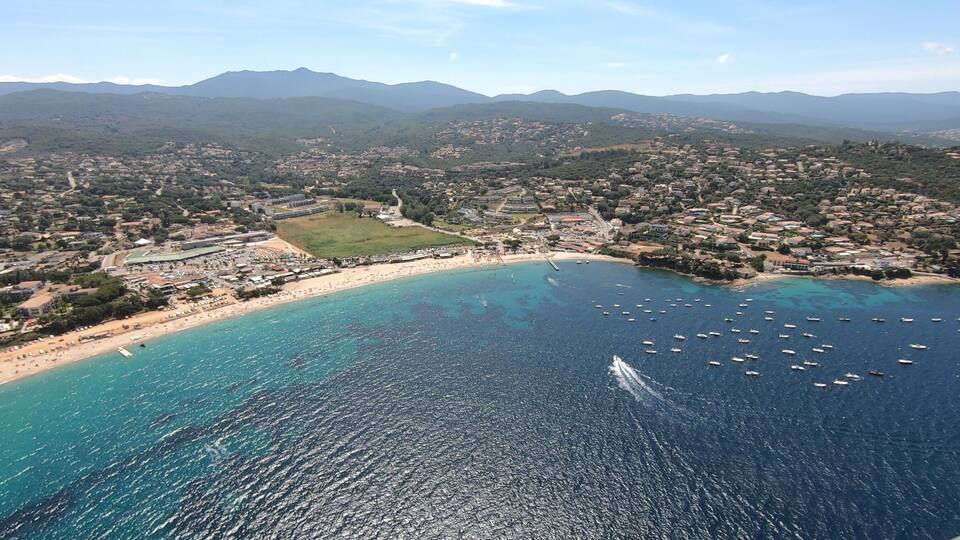 A coastal town with a beach, boats, and mountains in the background.