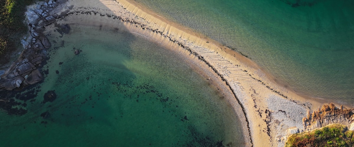 A coastal landscape with a sandy beach, clear turquoise waters, and rocky cliffs.