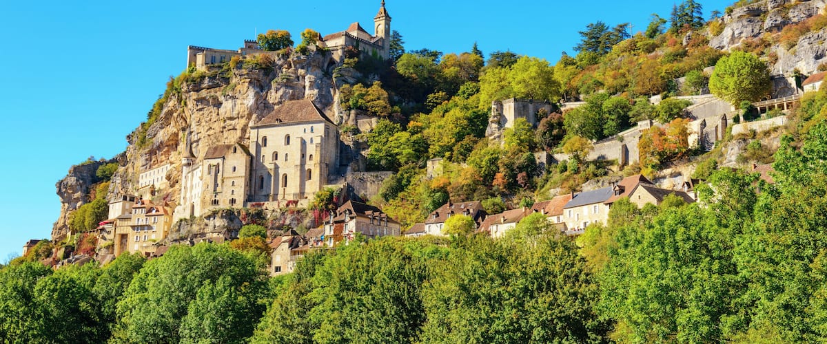 A historic castle perched on a rocky hill, surrounded by lush greenery and trees.