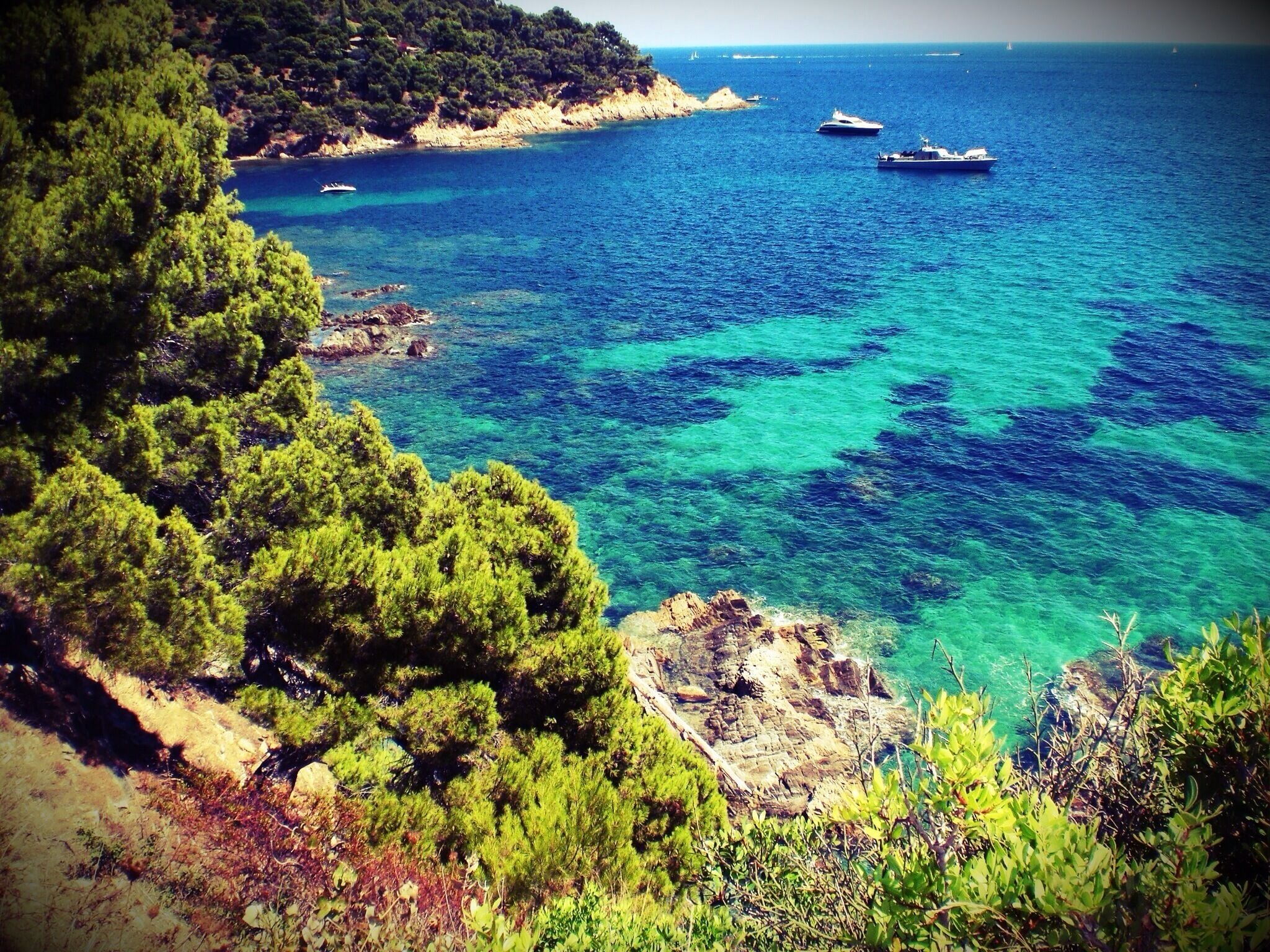 A coastal landscape with clear blue waters, rocky outcrops, and dense green trees.