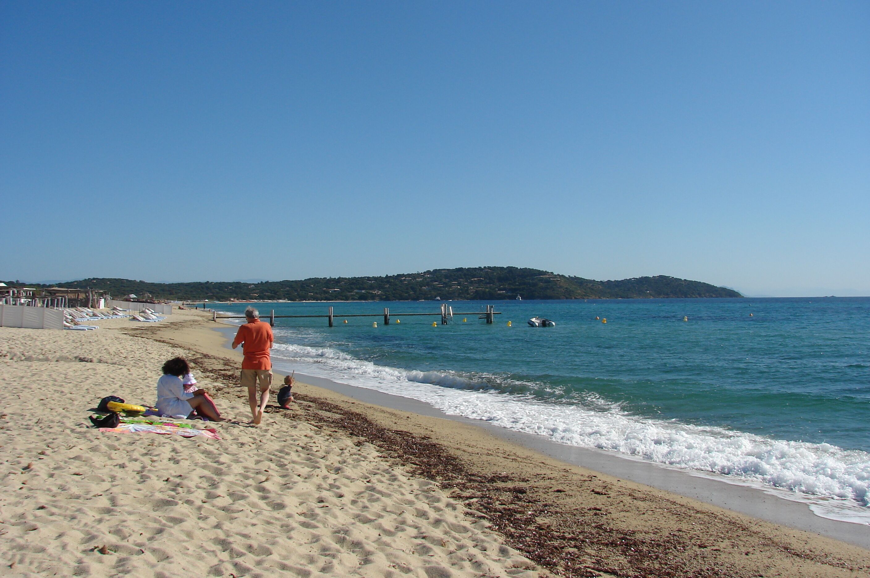 A sandy beach with people, a pier, and a distant hill.