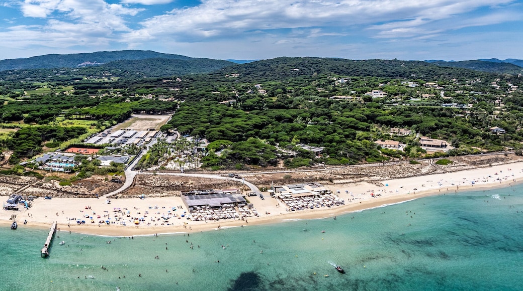 panoramic aerial landscape view of Pampelonne Beach - located at coastline of Ramatuelle, Côte d’Azur, France - with people on the beach and in water and green wooded hilly landscape in background