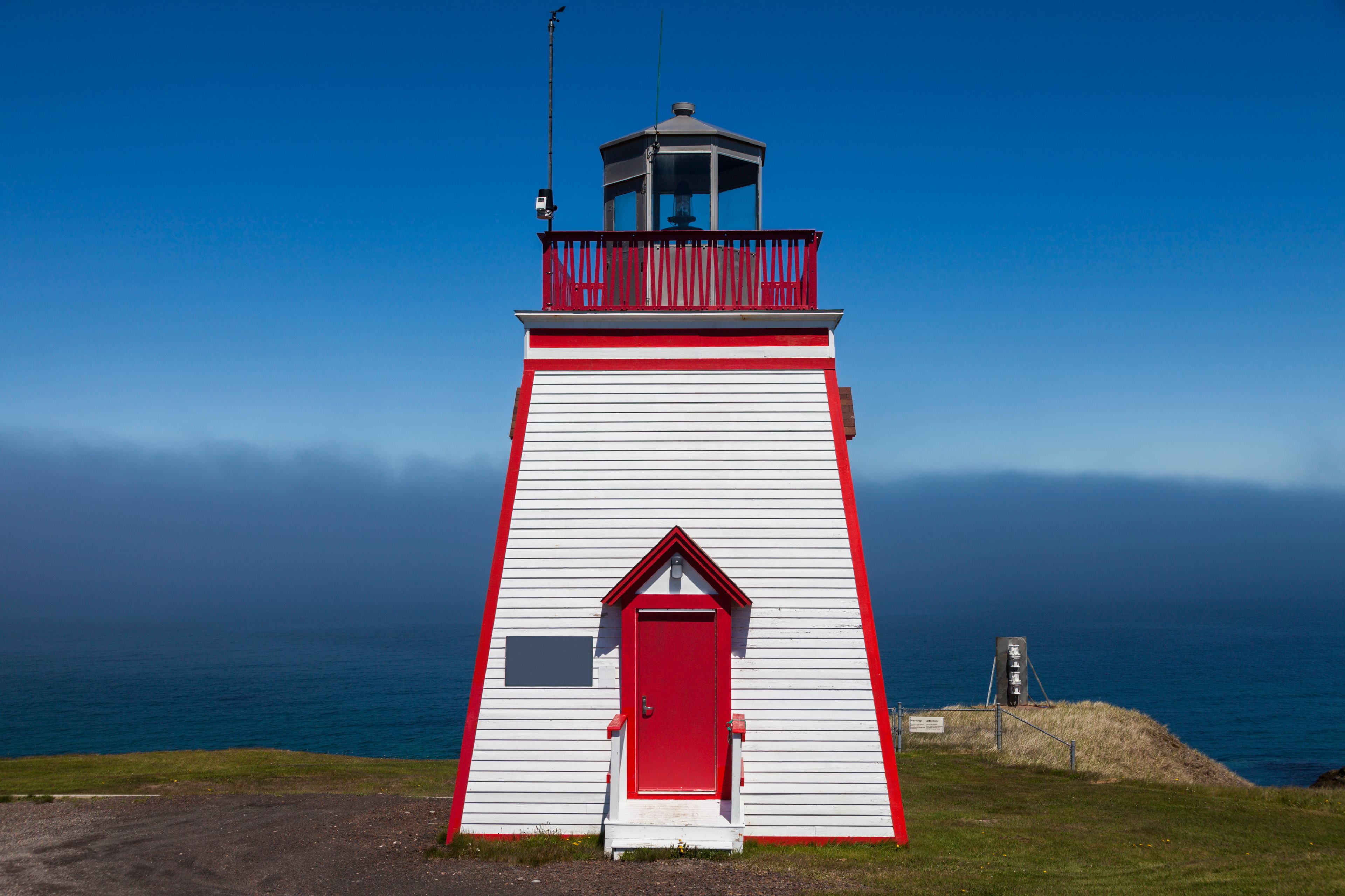 A lighthouse with a red and white facade, a balcony, and a clear view of the ocean in the background.